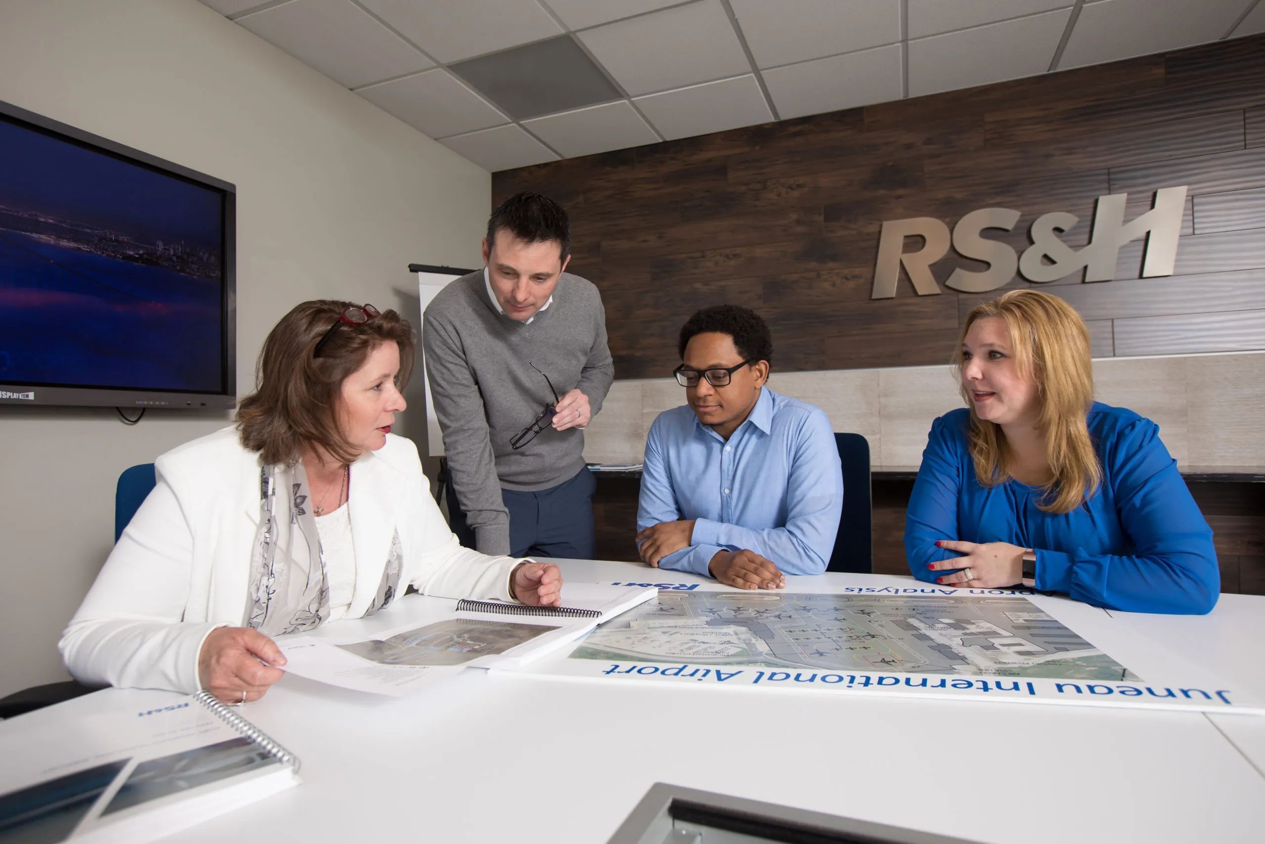 Four RS&H associates at a conference table. RS&H logo on wall in background.