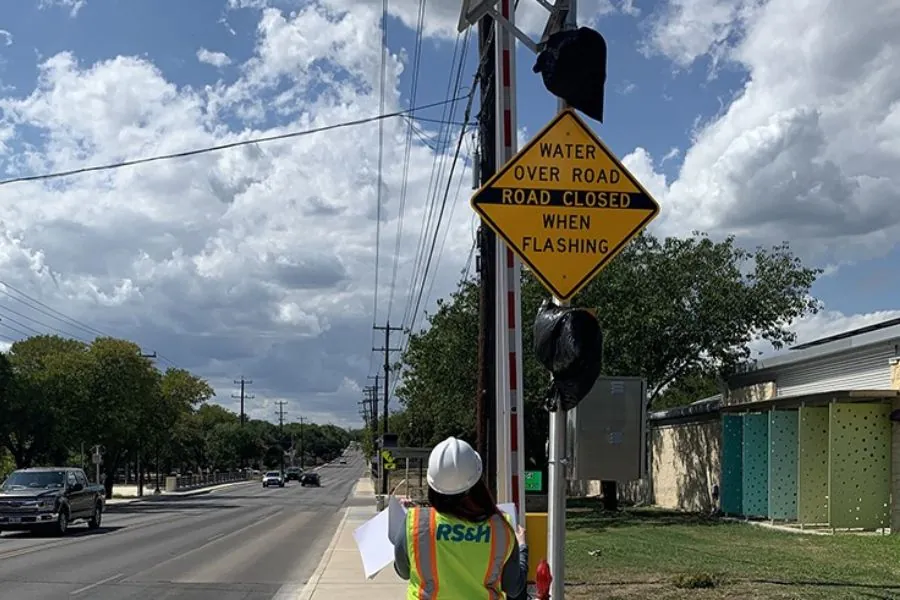 A lady in an RS&H hat standing next to a street sign.