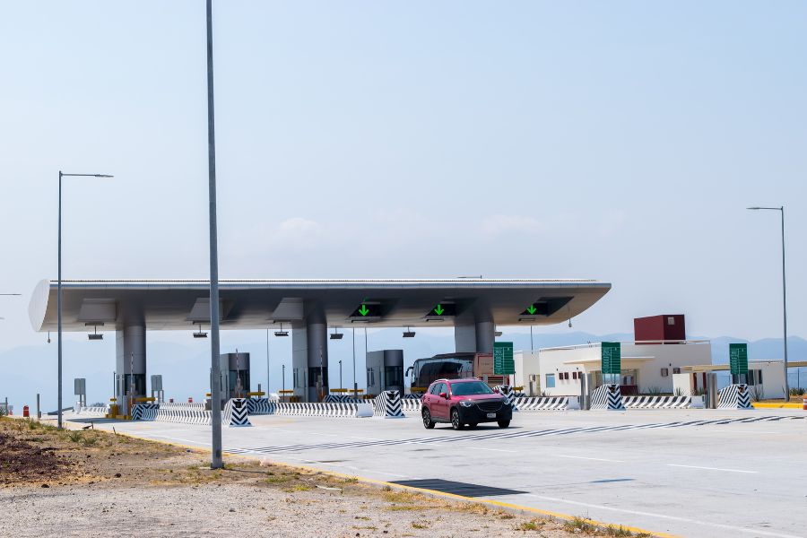 A red car driving away from a toll booth.