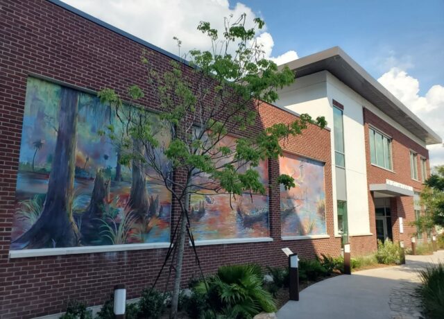 Brick building with colorful landscape murals and small tree in front.