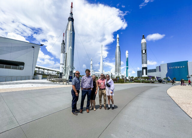 Group posing at Kennedy Space Center with rockets in background