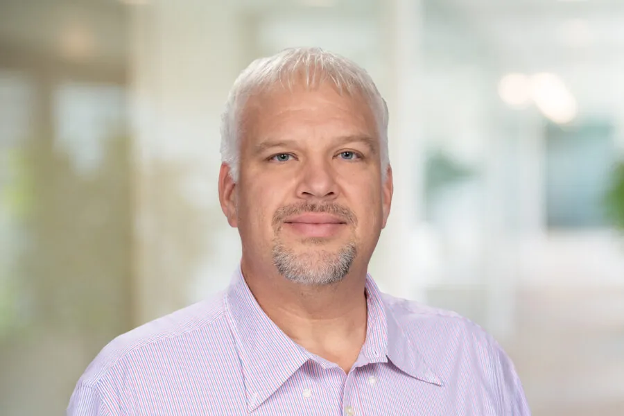 Barry Tim smiling in an office environment, wearing a light purple shirt