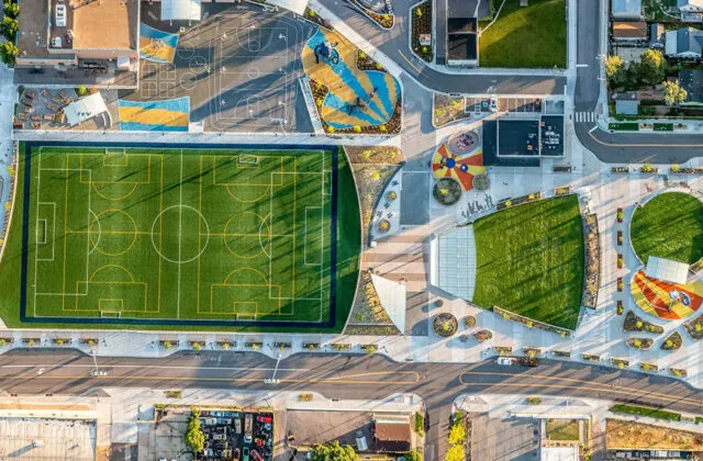 Aerial view of a sports complex featuring a soccer field, adjacent sports courts, surrounding green spaces, and colorful pathways