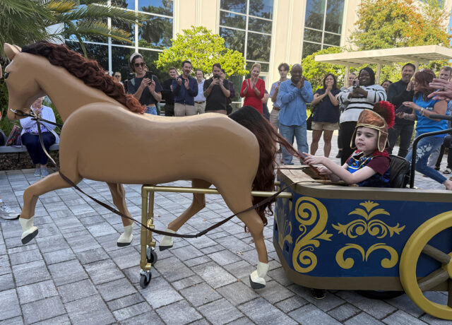 Child in Roman chariot costume with horse, crowd clapping in background