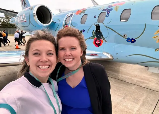 Two smiling women in front of blue airplane with floral artwork