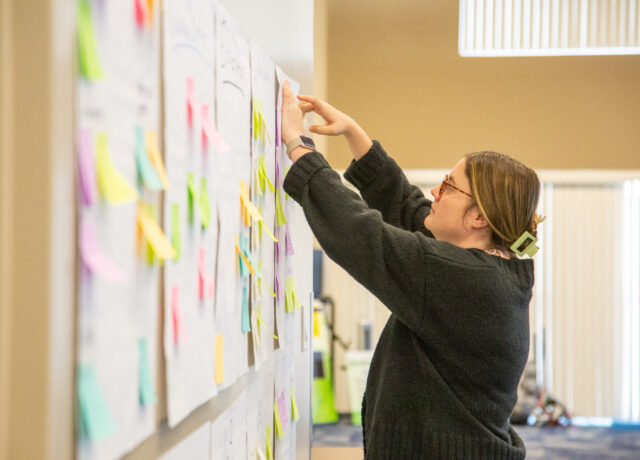Tara Pence arranging colorful sticky notes on a wall during a workshop