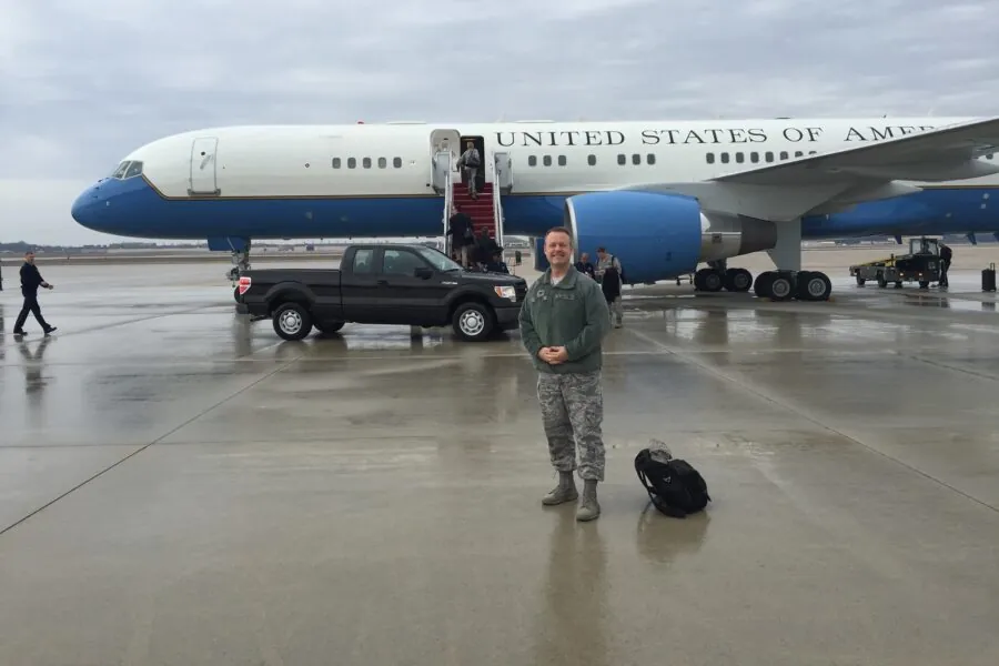 Man in military uniform stands in front of "United States of America" plane on tarmac