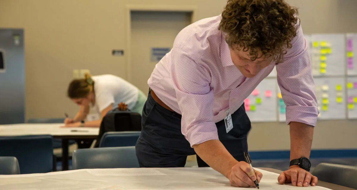 Aaron Briggs leaning over a table, writing on a large paper, during a planning session