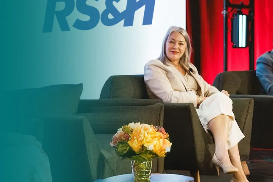 Lisa seated on a stage, smiling; RS&H sign behind her
