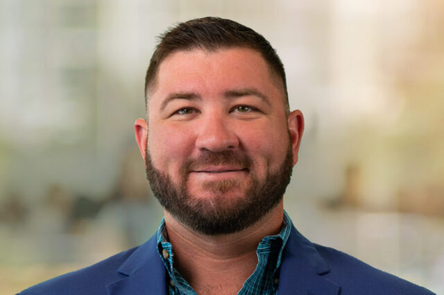 Brent Wilkins smiling, wearing a blue blazer with a blurred background.