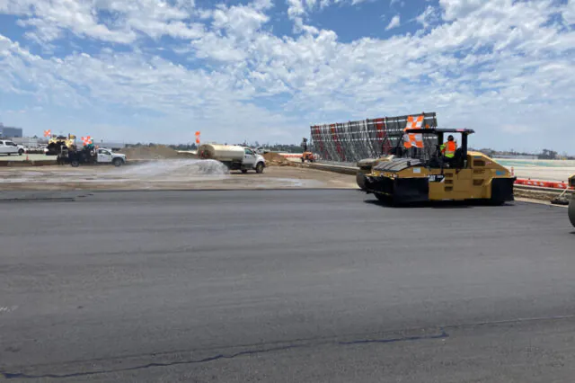 Construction vehicles and workers on airport taxiway under clear sky.