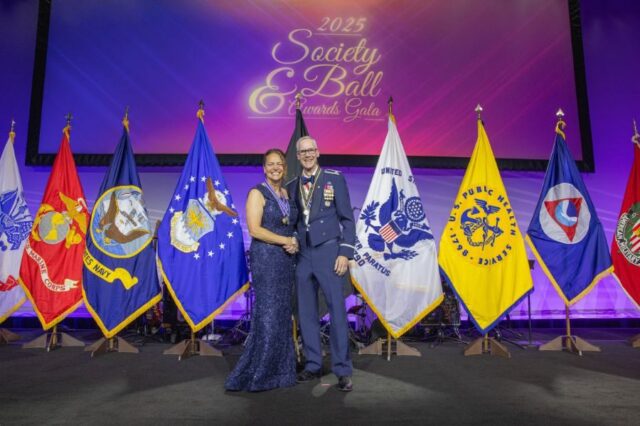 Man and woman smiling, wearing medals, in front of military flags. '2025 Society & Ball Edwards Gala' text above.