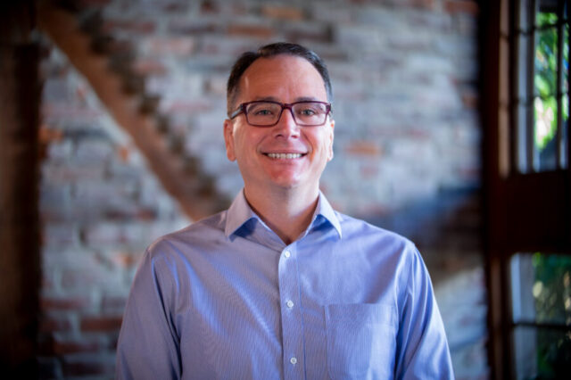 Steve Creamer smiling in front of a brick wall background