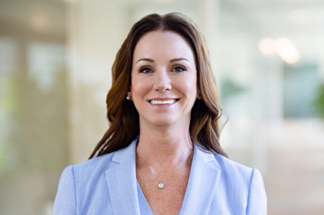 Holland Kim smiling in a light blue blazer, blurred office background
