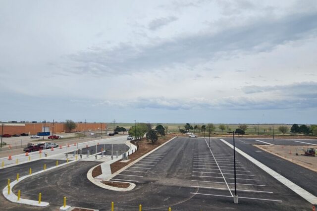 Newly paved parking lot under overcast sky with distant trees