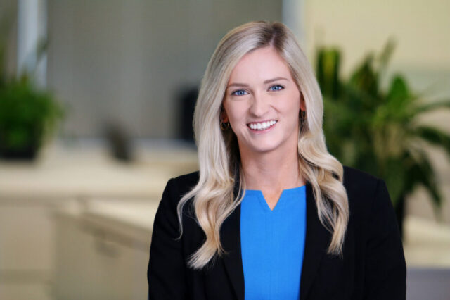Courtney smiling in an office setting, wearing a blue top and black jacket