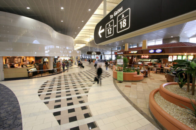 Spacious airport terminal with patterned flooring, various eateries, and signage indicating gates A12 to A18 directions