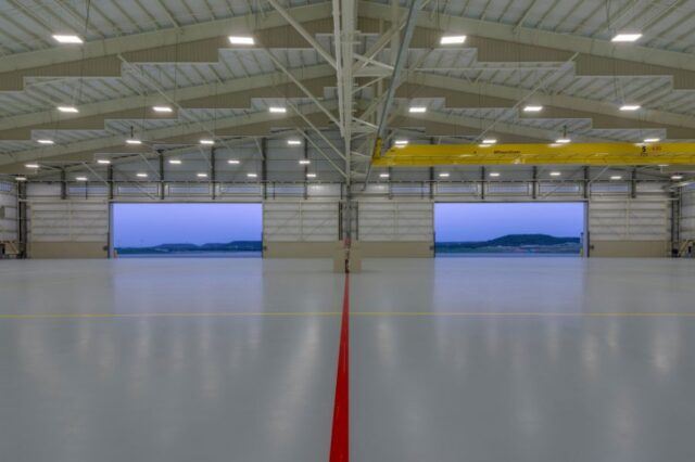 Wide interior view of an aircraft hangar with open doors revealing a twilight sky and distant hills