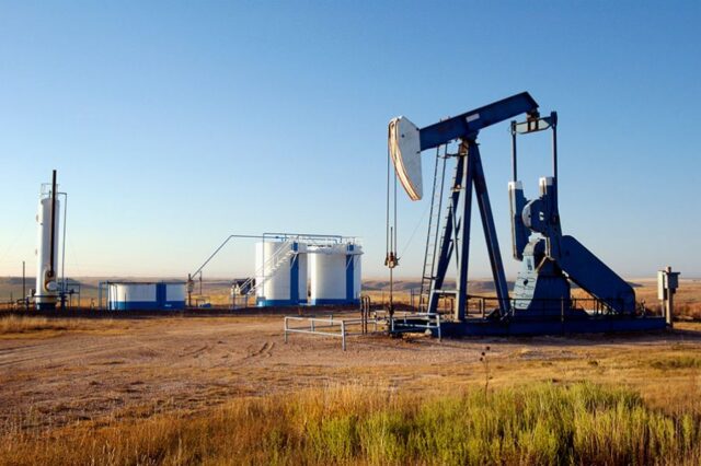 Oil pump jack and storage tanks in a barren landscape under a clear blue sky