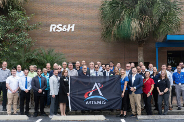 Group of people at RS&H building holding an Artemis program banner, smiling.
