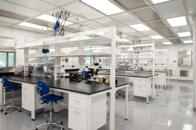 Bright, clean laboratory with white shelves and blue chairs, featuring microscopes and scientific equipment on black countertops