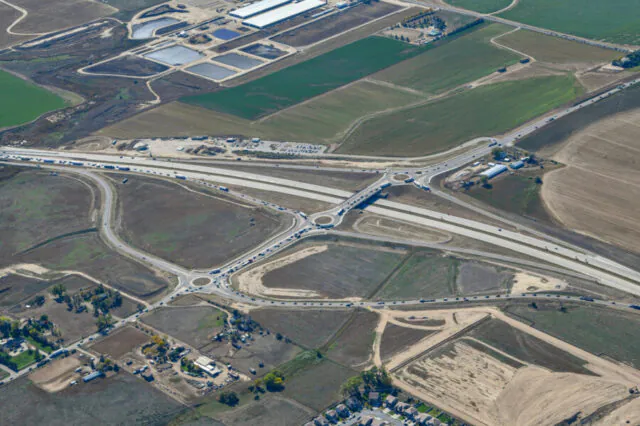 Aerial view of a roundabout interchange at I-25 and CO-402, surrounded by farmland.