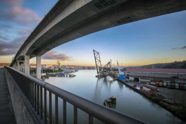 Bridge spanning over Seattle harbor at sunset, with cranes and docked boats
