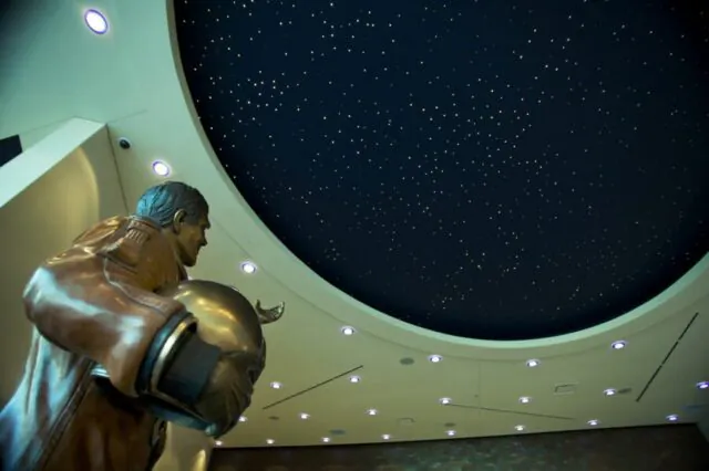 Astronaut statue beneath a star-like ceiling in a modern building.