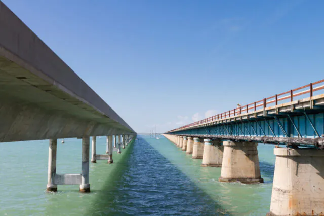 Two parallel bridges over turquoise water under a clear blue sky.