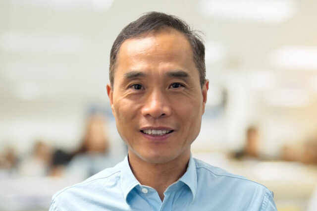 Gu Jim smiling in an office setting, wearing a light blue shirt.