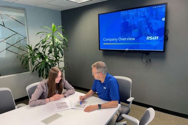 Man and woman discussing maps, "Company Overview" on screen, RS&H logo