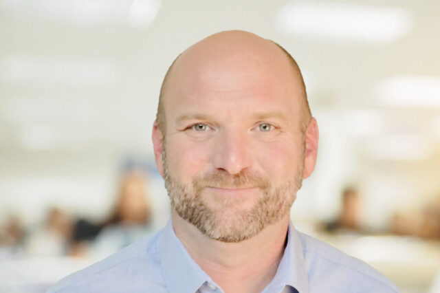 Curtis smiling in an office environment with blurred background.