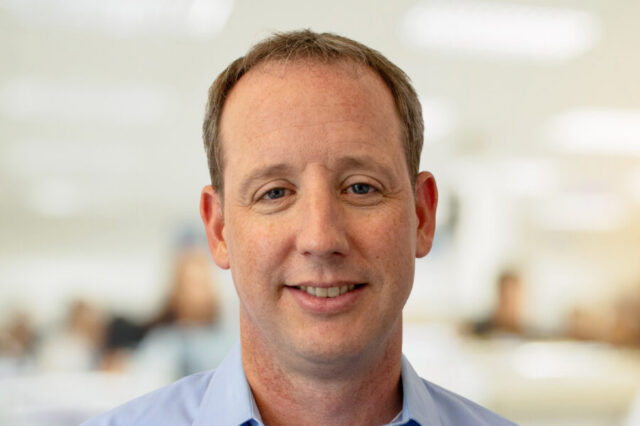 Jeremy Adams smiling in office setting, blurred background
