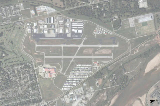 Aerial view of an airport layout with runways, buildings, and surrounding roads and river.
