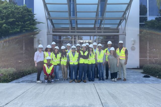 Group of people in safety vests and helmets standing outside a building entrance