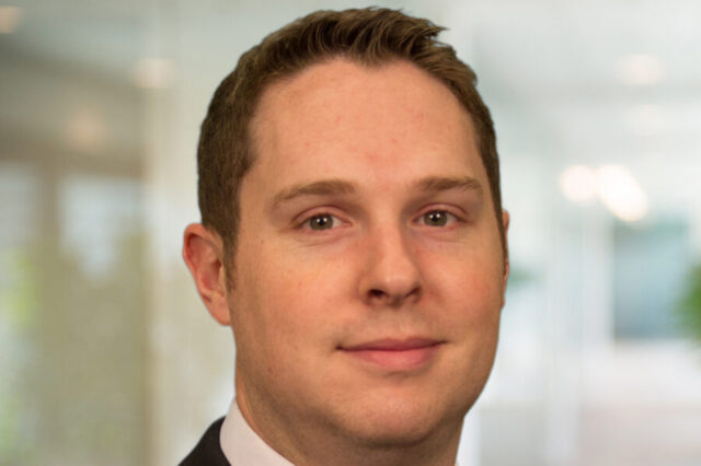 Clayton Singleton in a business suit, neutral expression, blurred office background